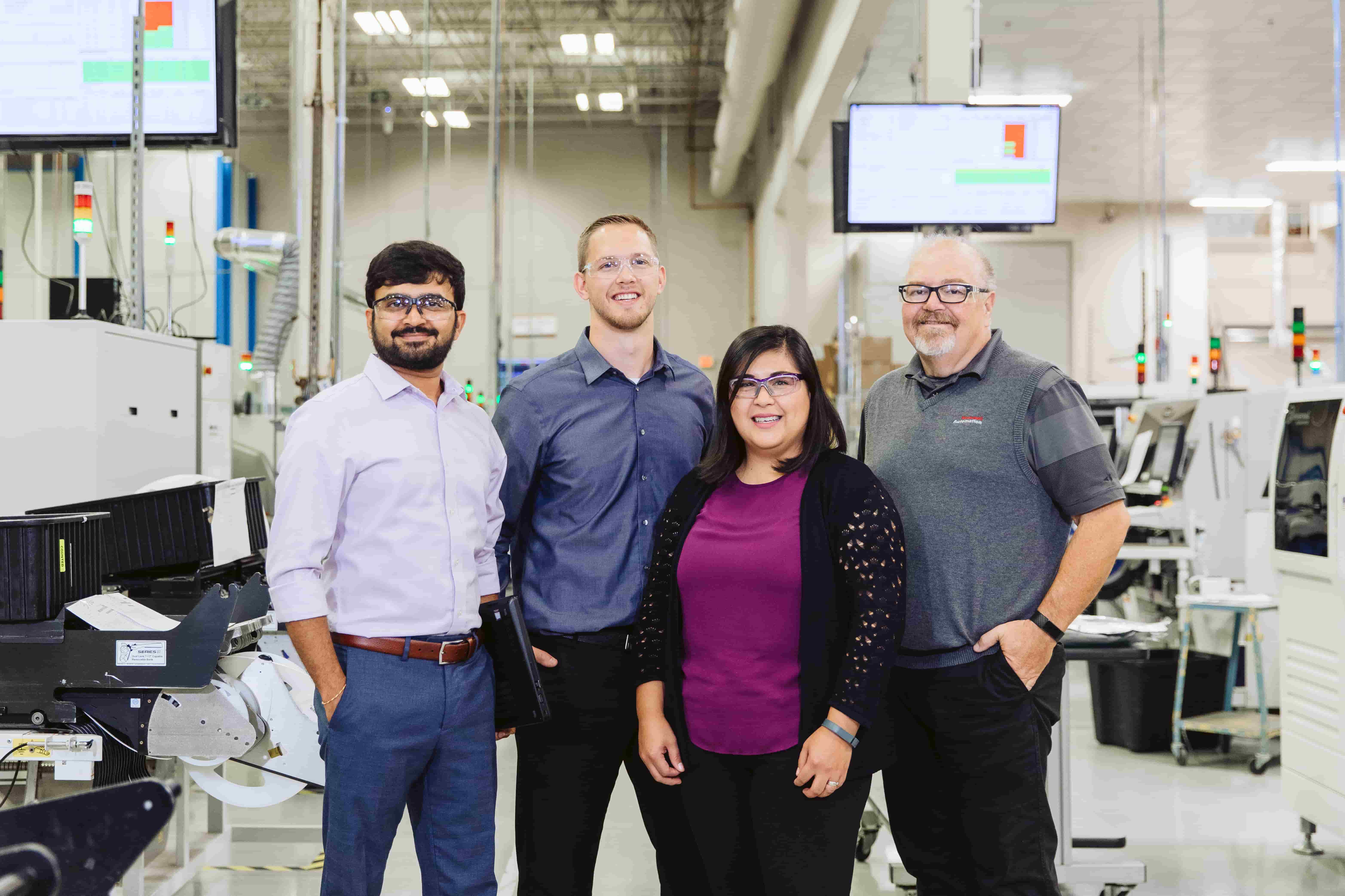 Team members stand side-by-side in factory Team members stand side-by-side in factory